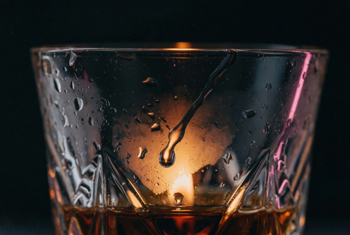 Whiskey glass with water droplets and warm amber backlight, symbolizing sitting with difficult emotions and processing jealousy