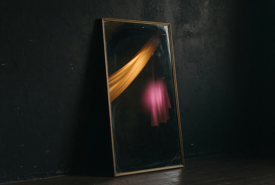 Antique mirror leaning against a dark wall with abstract blurred light reflection, representing self-reflection on jealousy and identity